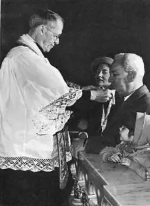 The ceremony of investiture in the Miraculous Medal is held after each service. Father Skelly is shown investing a family.